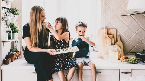 A mom sits next to her kids sharing a snack