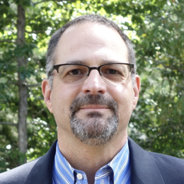 a man wearing a suit and tie smiling at the camera